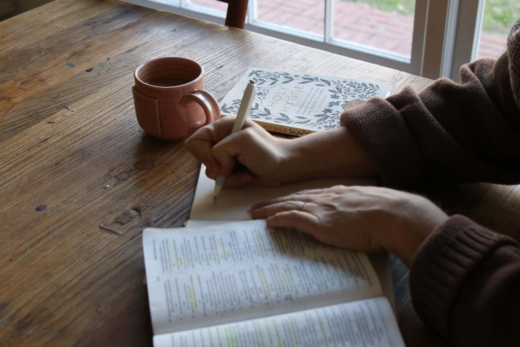 Woman journaling with a pen, Bible, and mug of coffee